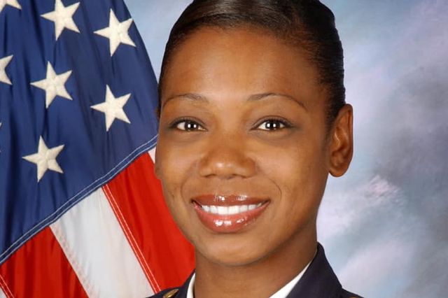 Photograph of Keechant Sewell smiling at the camera in front of a US flag